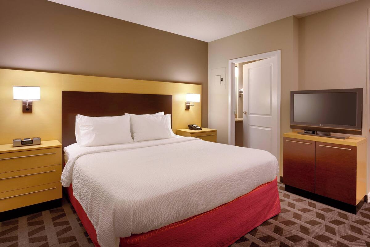 A hotel room with a large bed, bedside lamps, a TV, a wardrobe, and a door.