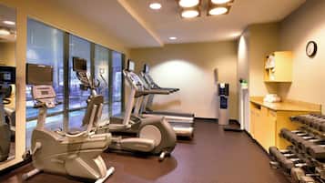 Une salle de sport équipée de tapis de course, de vélos elliptiques et d’haltères.