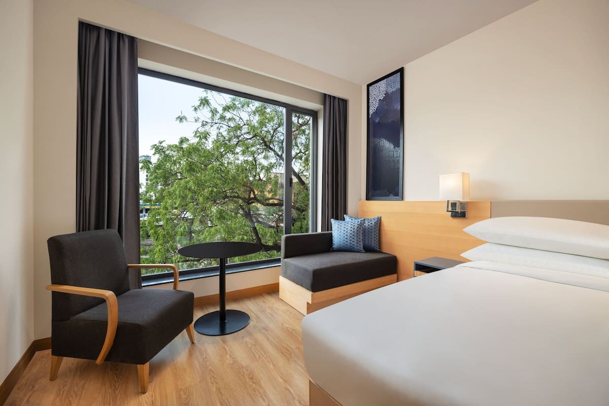 A hotel room with a bed, a sofa, a chair, a small table, and a window with curtains.