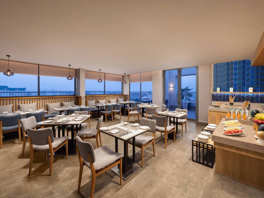A modern restaurant with high ceilings, large windows, and a view of the cityscape.