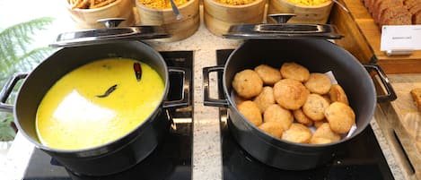 A buffet with various dishes including a pot of yellow curry, fried items, and a sign for 'Banana Cake'.