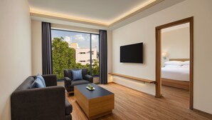 Ein modernes Hotelzimmer mit einer Sitzecke, einem Couchtisch, einem Fernseher und einem großen Fenster mit Blick auf die Stadt.