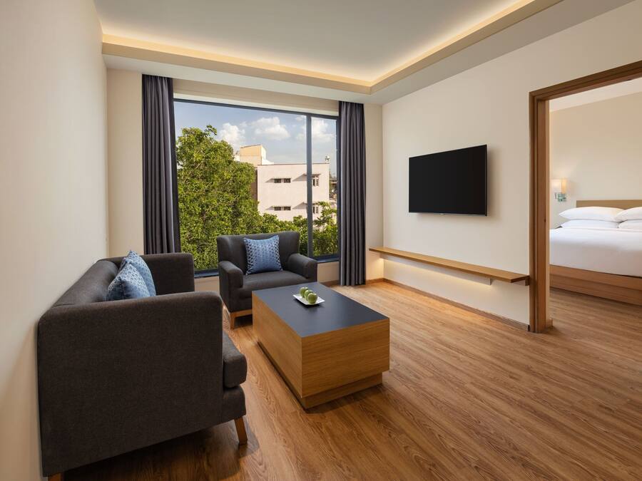 Habitación de hotel moderna con sofá, una mesita de centro, televisión y una ventana grande con vistas a la ciudad.