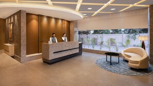 Ein moderner Empfangsbereich mit einer Rezeption, zwei Mitarbeitern, einem bequemen Lounge-Sessel und einem großen Fenster mit Blick ins Freie.