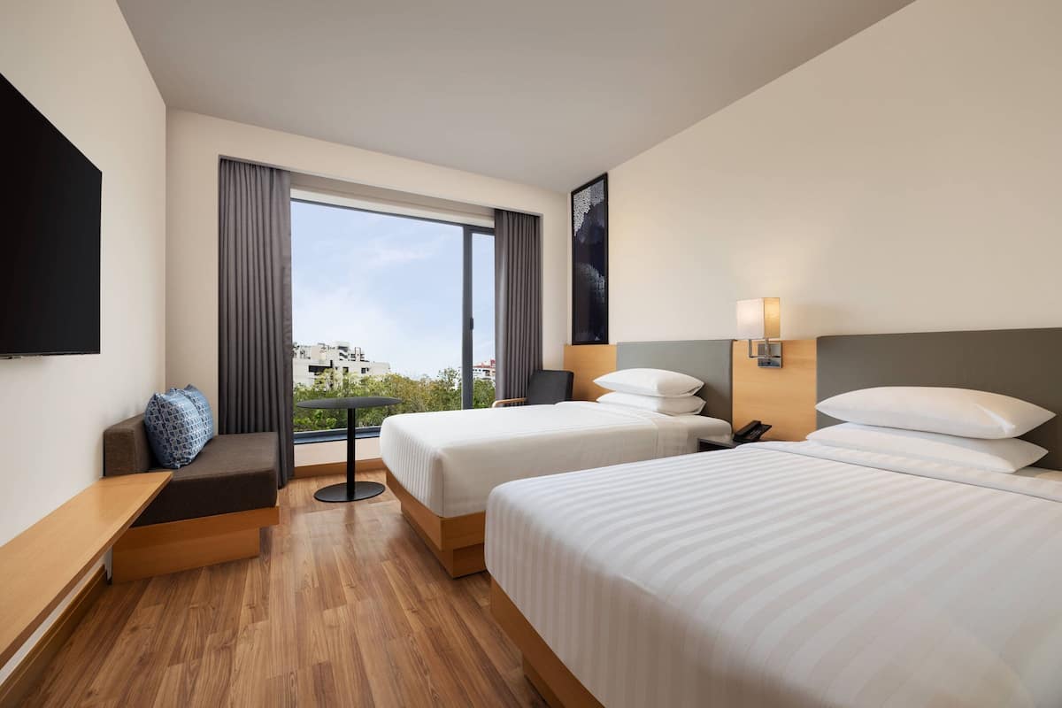 A hotel room with two beds, a sofa, a TV, a desk, and a window with curtains.