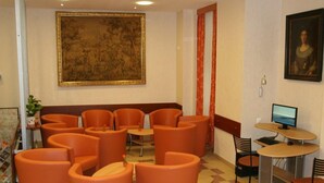 A lobby with orange seating, a large framed painting, a computer, and a desk with a monitor. - Hotel Terminus Vienna (Vienna)