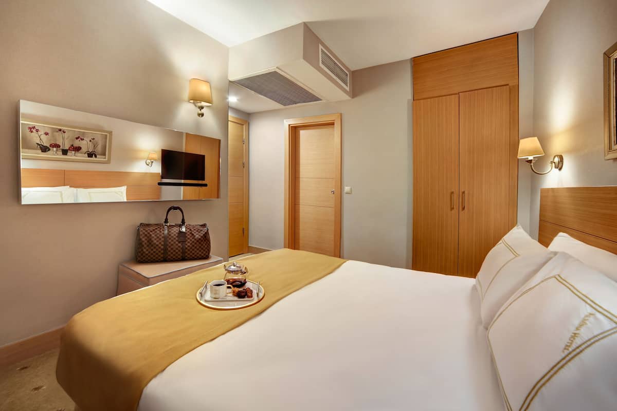 A hotel room with a bed, a TV, a desk with a lamp, a wardrobe, and a mirror.