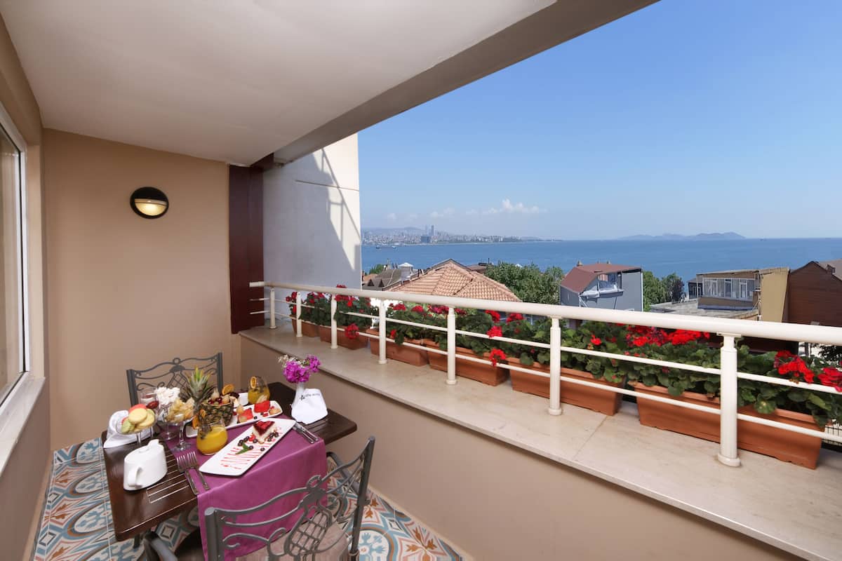 A balcony with a table set for breakfast, potted plants, and a view of the sea and city skyline.