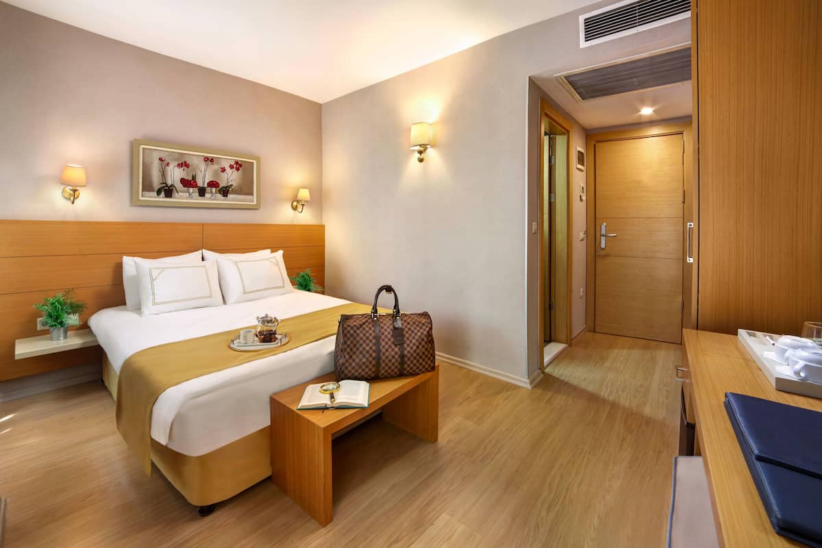 A hotel room with a bed, bedside table, lamp, and a door.