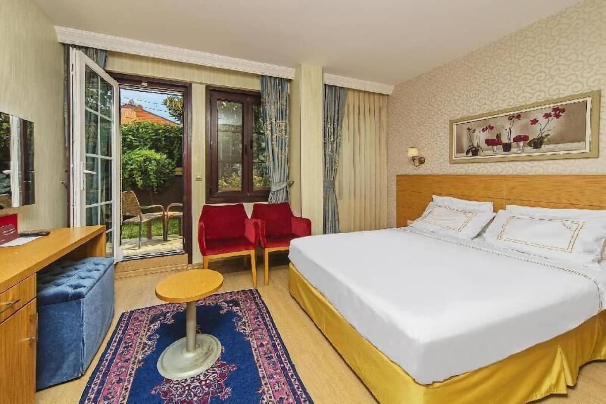 A hotel room with a bed, a desk, a chair, a small table, and a view of the outdoors.