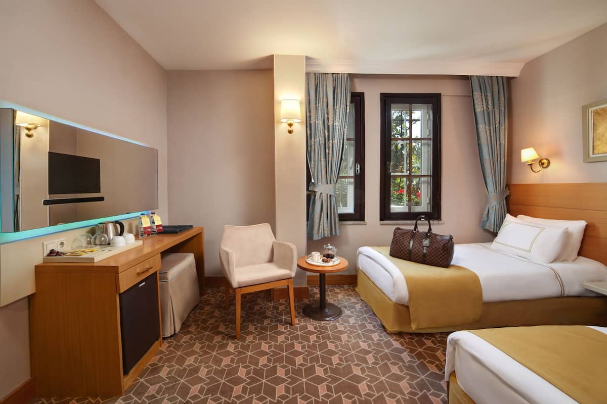 A hotel room with a bed, a desk with a mirror, a chair, a small table, and a window with curtains.