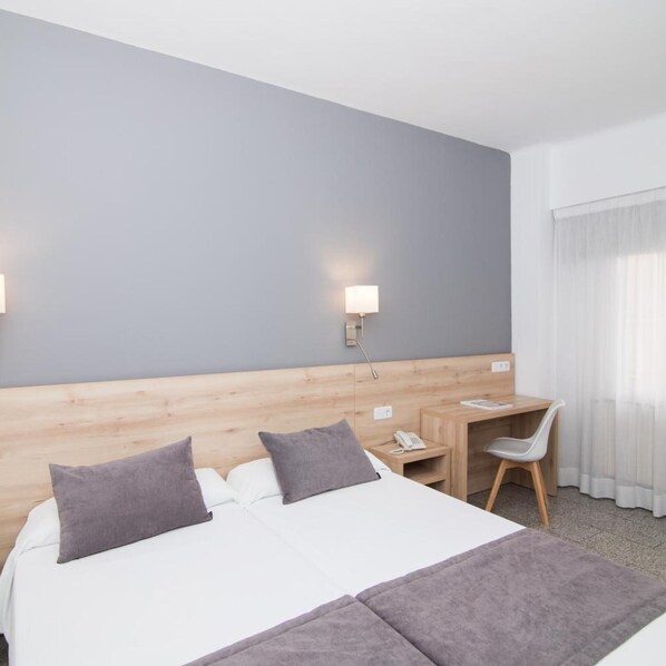 Una habitación de hotel con cama, mesita de noche, lámpara y escritorio con silla.