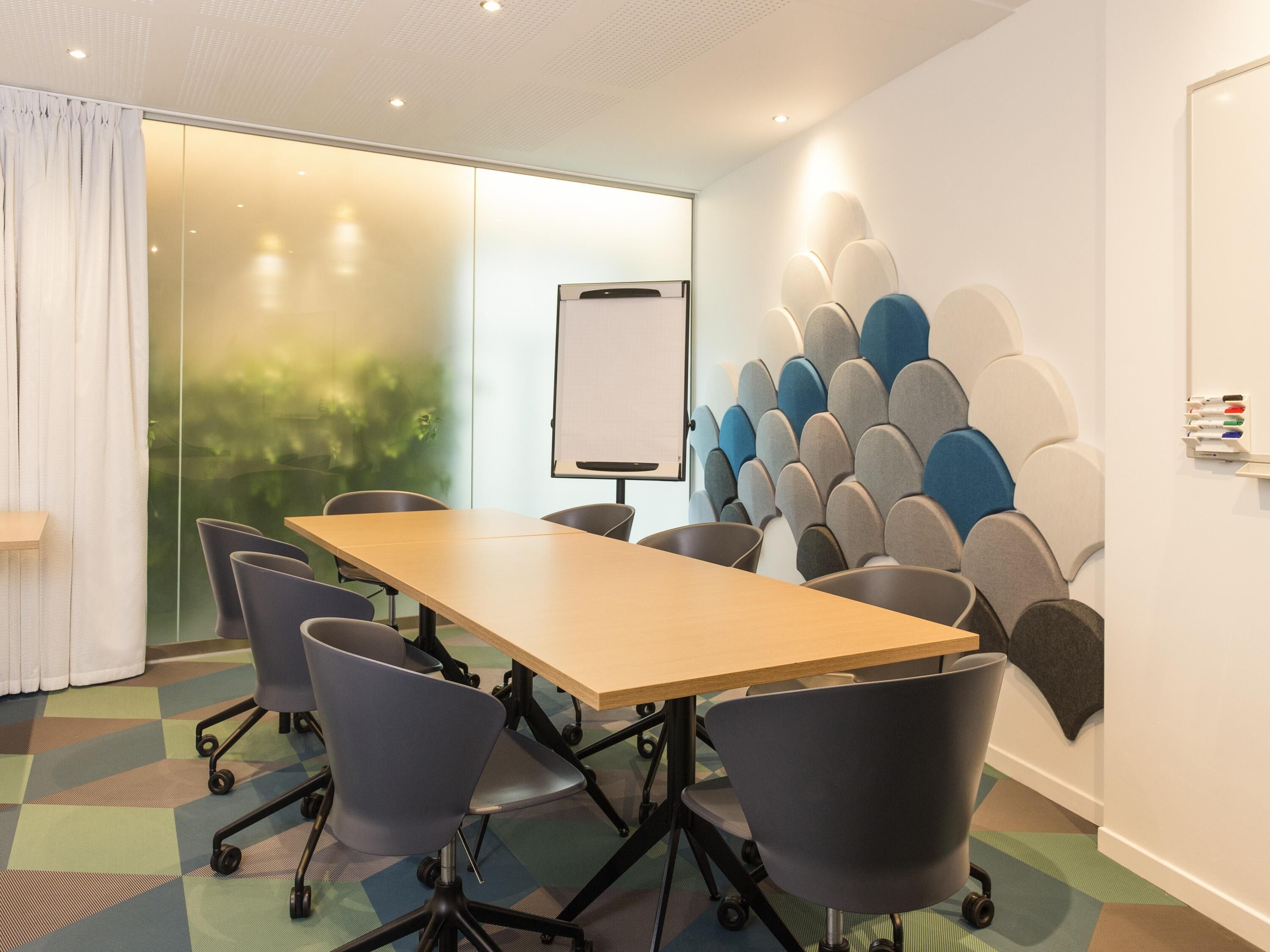 Un salón de conferencias con una larga mesa, cuatro sillas, una pizarra y una pared con un diseño único.