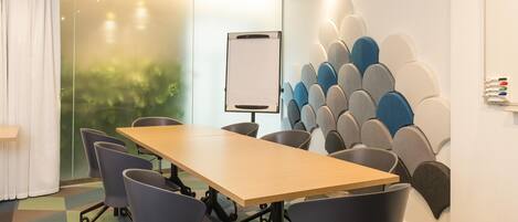 Un salón de conferencias con una larga mesa, cuatro sillas, una pizarra y una pared con un diseño único.