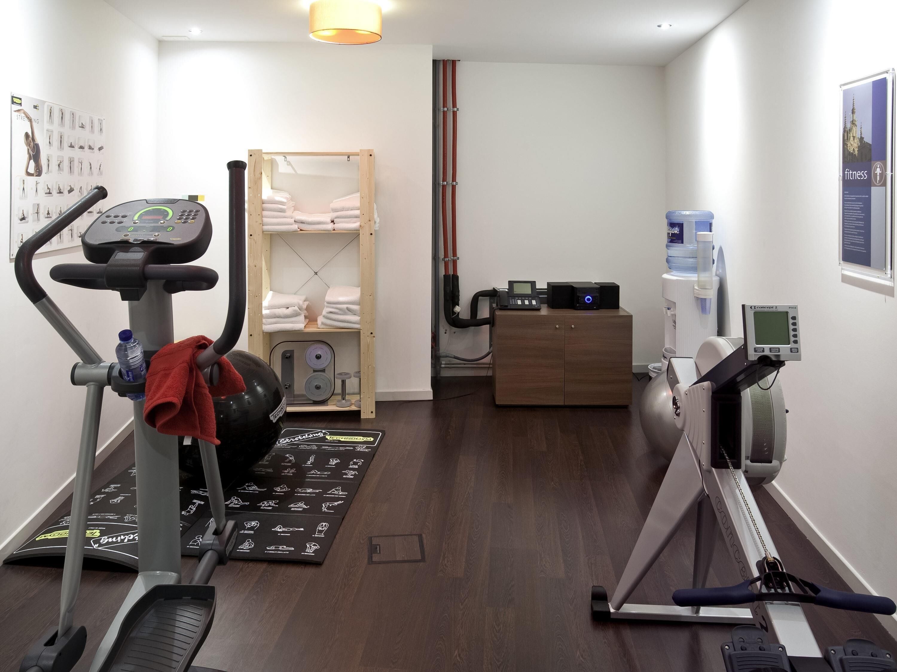 Ein Fitnessraum mit Trainingsgeräten, einer Holztruhe und einem Poster an der Wand.