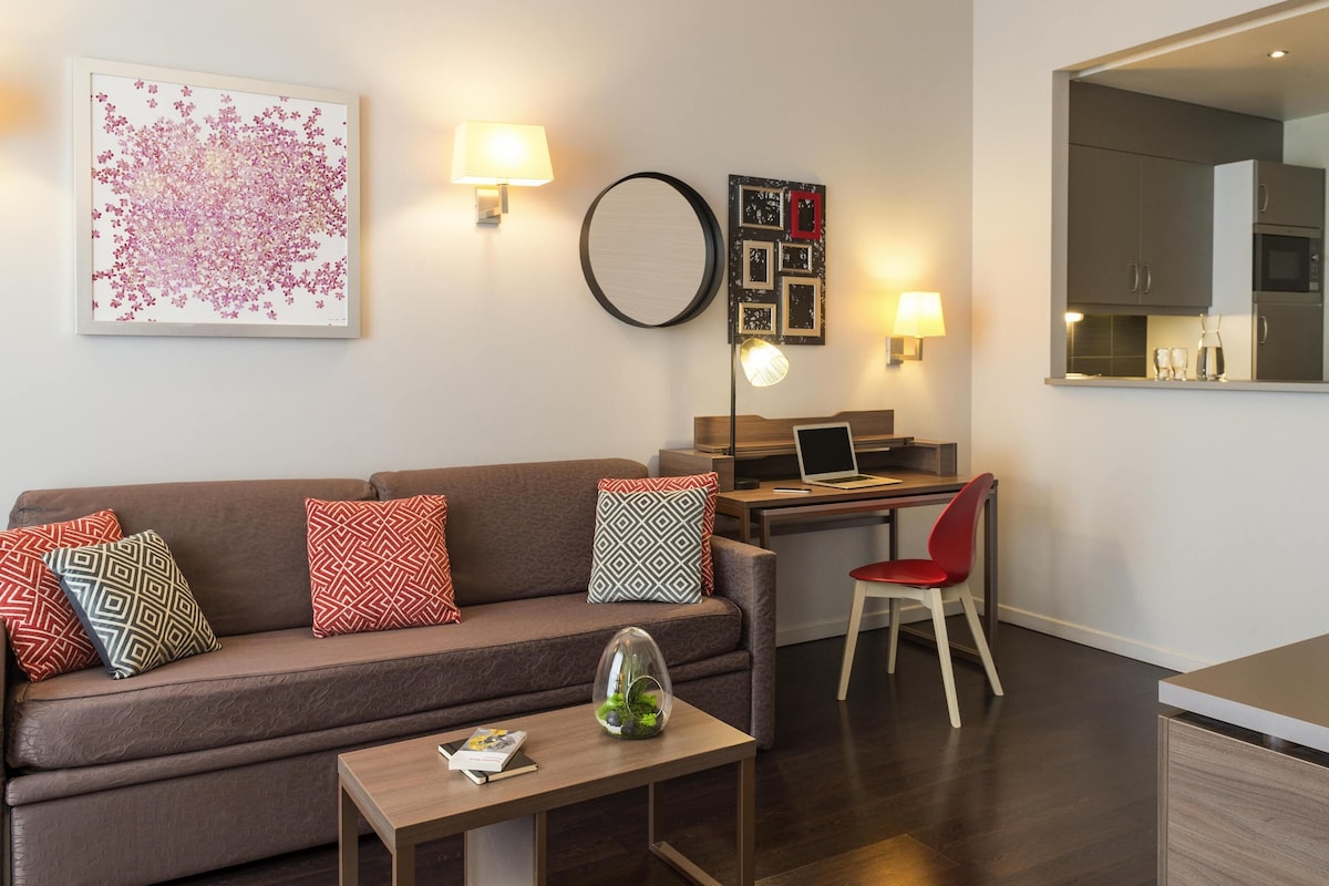 Een moderne woonkamer met een bank, een bureau, een laptop en een eethoek.