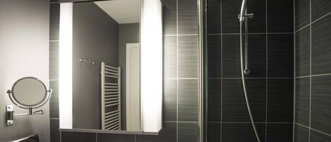 Une salle de bain moderne avec un lavabo blanc, un miroir rond, une douchette à main et des murs recouverts de carreaux foncés.