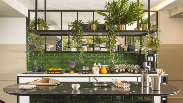 Une cuisine moderne avec un revêtement mural vert, un plan de travail noir, ainsi que divers appareils de cuisine et ustensiles.