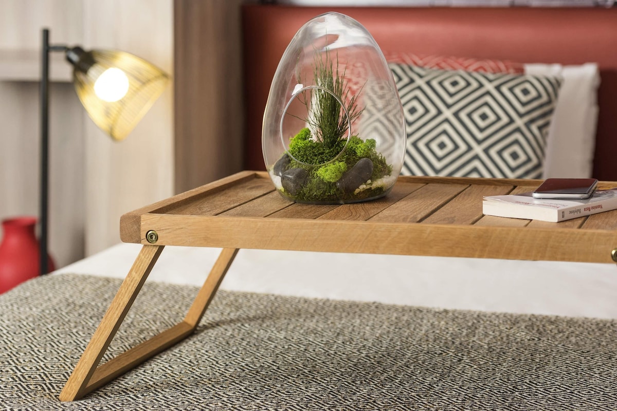 Een glazen terrarium met groene planten en stenen op een houten dienblad.