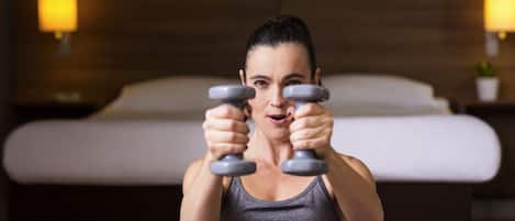 A person exercising with dumbbells in a room with a bed and wall-mounted lamps.