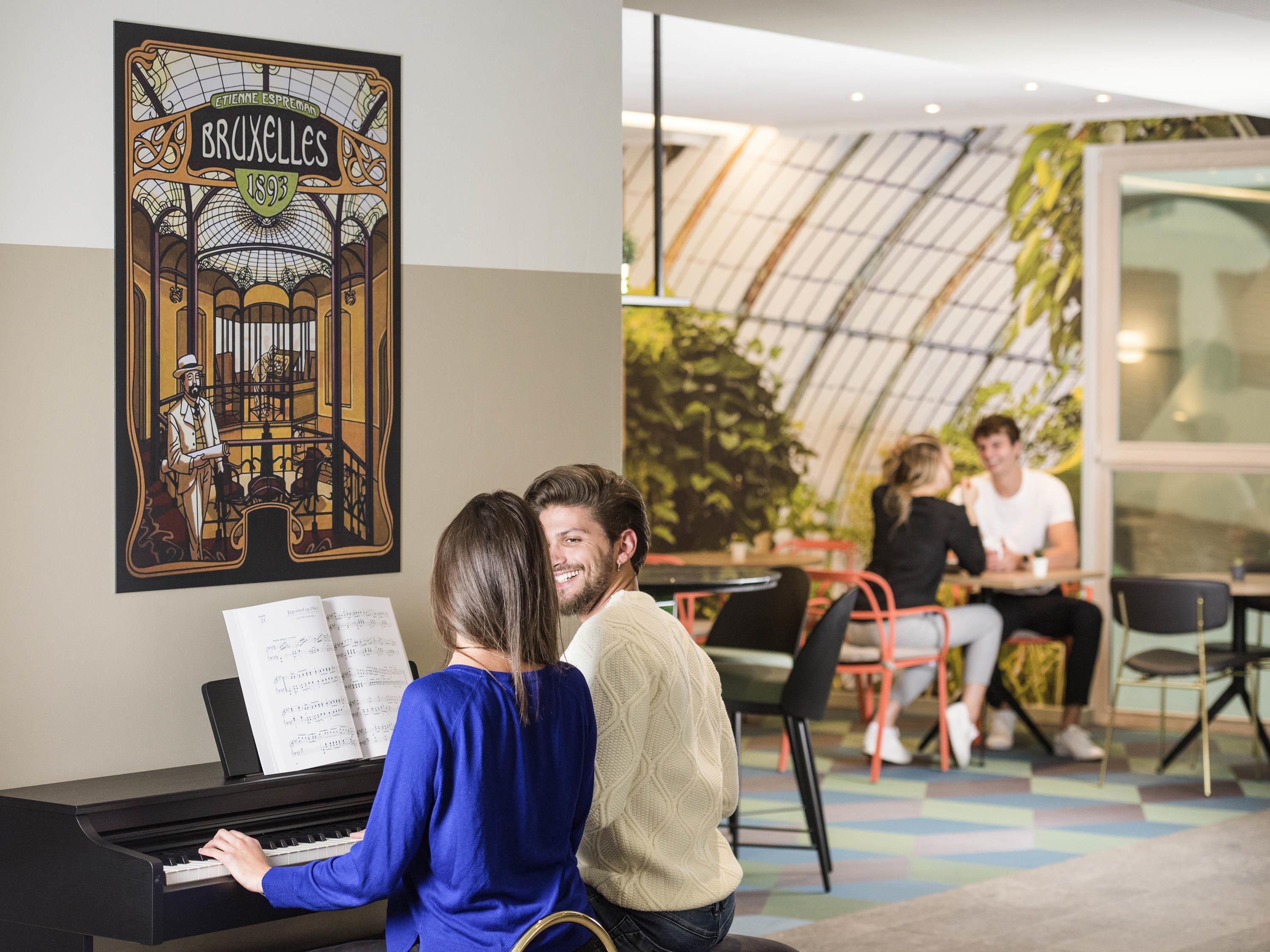 A piano with sheet music, a couple sitting together, and a café area with people in the background.