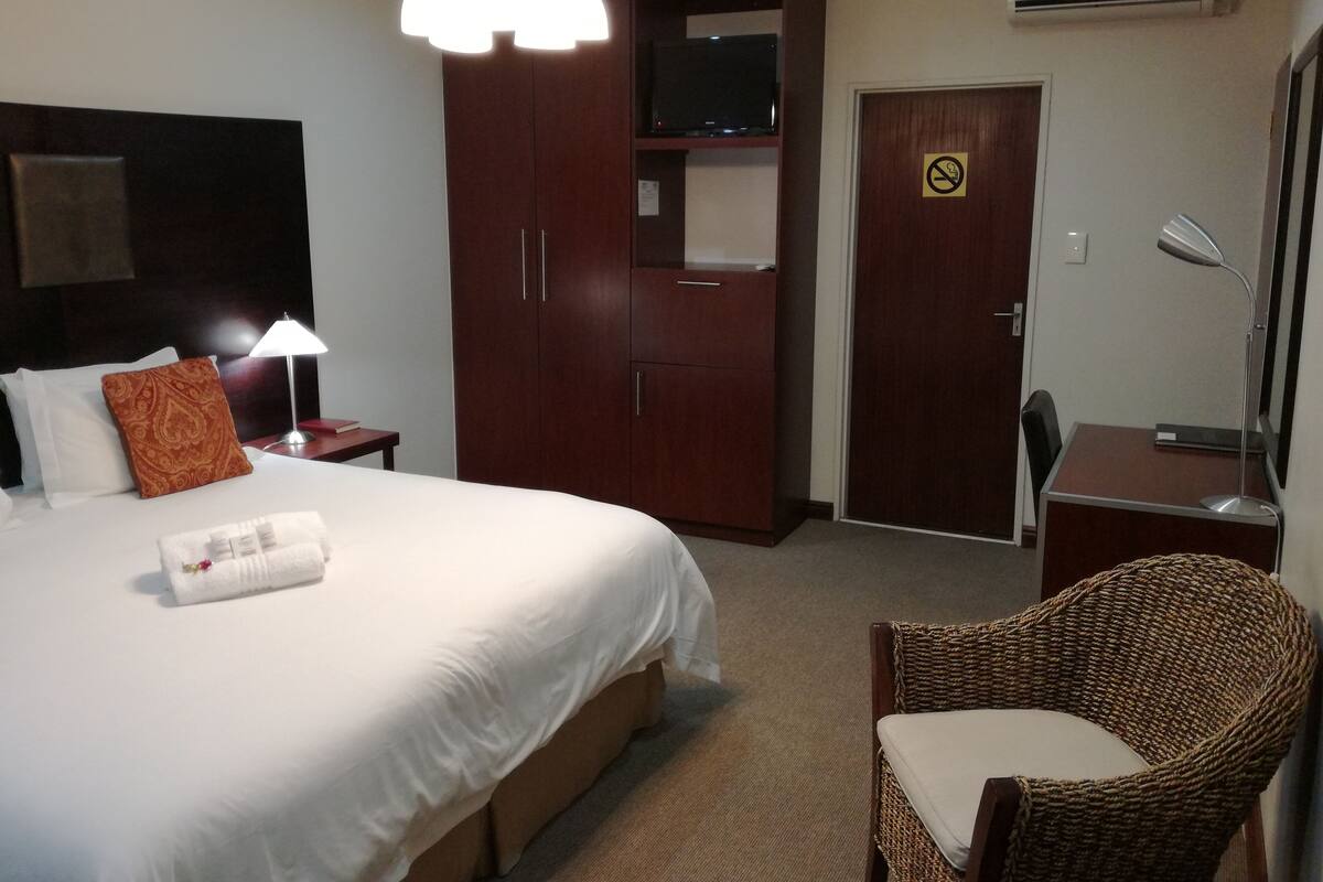 Ein Hotelzimmer mit einem großen Bett, einem Schreibtisch mit Stuhl, einem Fernseher und einem Kleiderschrank.