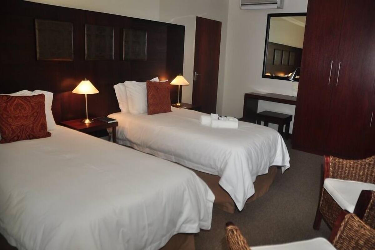 Ein Hotelzimmer mit zwei Einzelbetten, Nachttischlampen, einem Schreibtisch, einem Stuhl und einem Spiegel an der Wand.