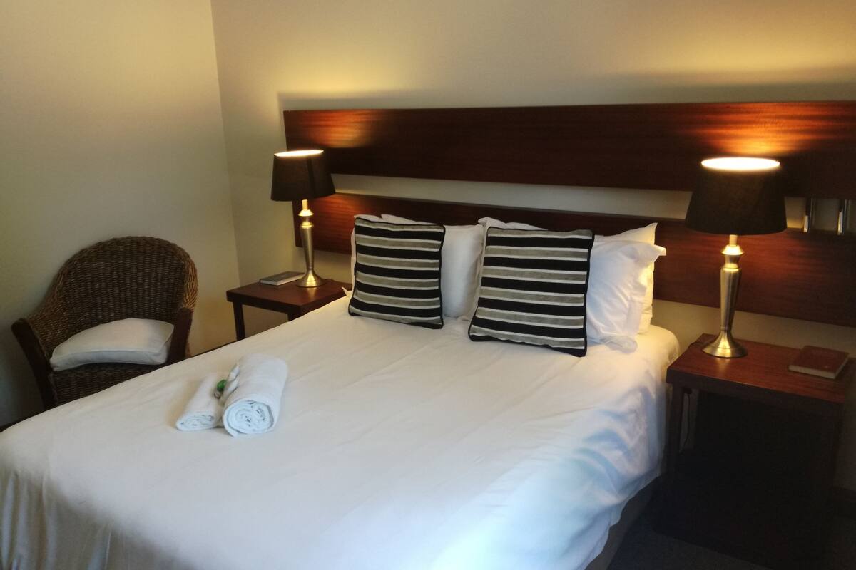 Ein Hotelzimmer mit einem großen Bett, zwei Nachttischen, einem Sessel und zwei Lampen.