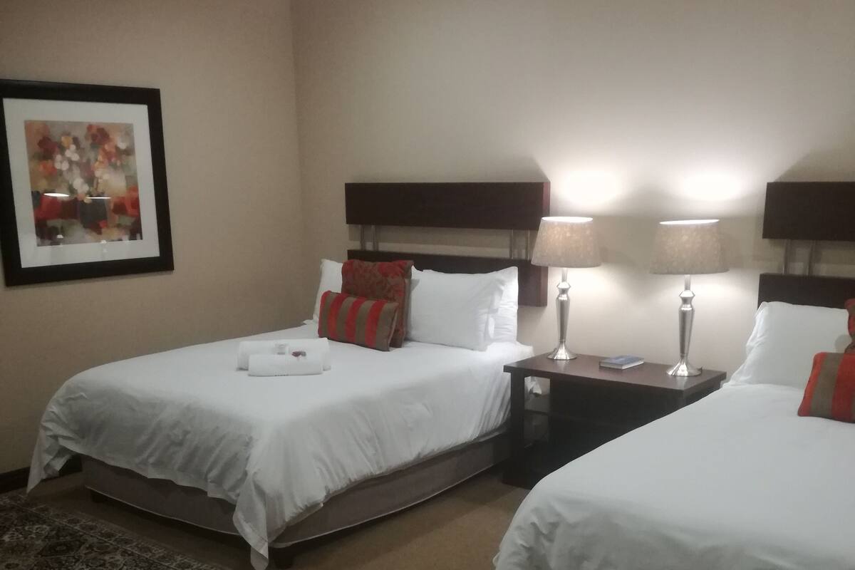 Ein Hotelzimmer mit zwei Betten, einem Nachttisch, einer Lampe und einem gerahmten Bild an der Wand.