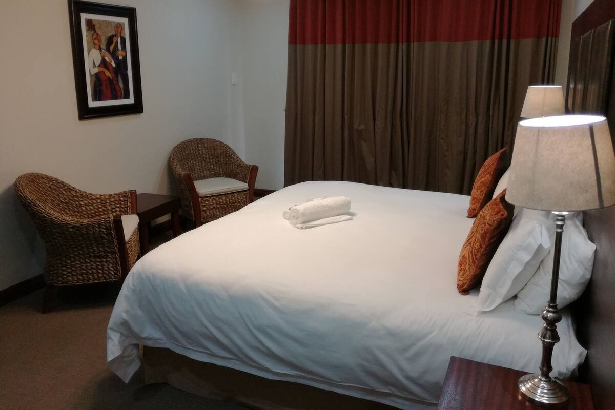Ein Hotelzimmer mit einem Bett, zwei Korbstühlen, einem Tisch mit Lampe und einem Bild an der Wand.