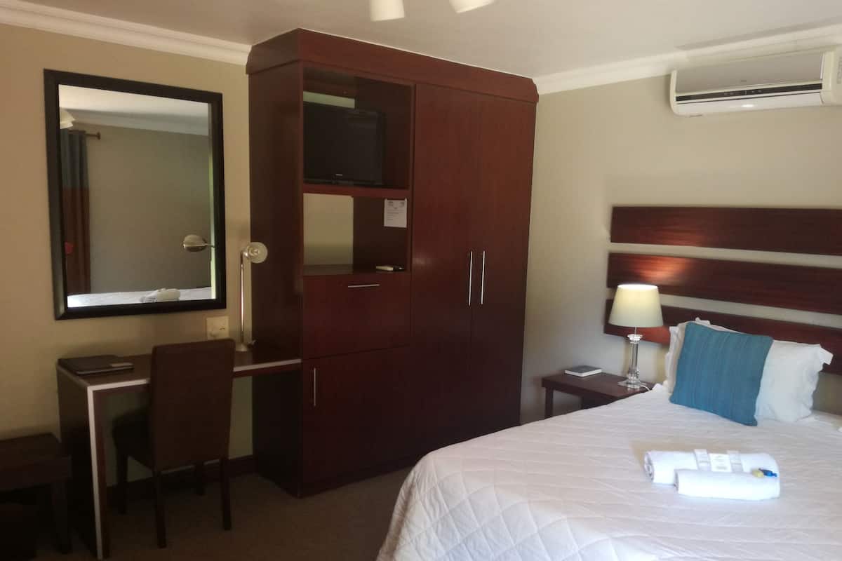 Ein Hotelzimmer mit Bett, Schreibtisch, Kleiderschrank, Spiegel und Klimaanlage.