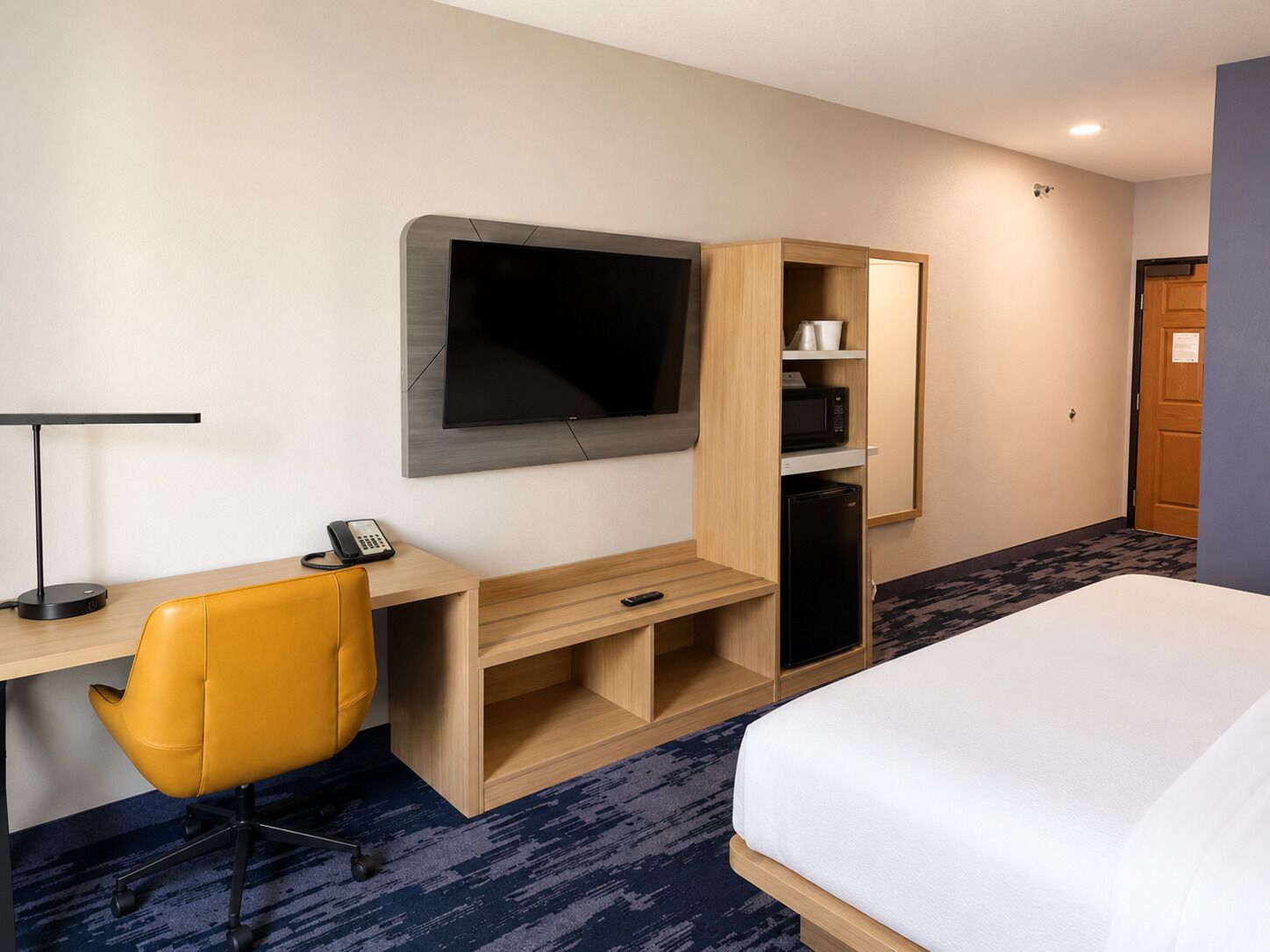 A hotel room with a bed, a desk with a chair, a television, a microwave, and a refrigerator.