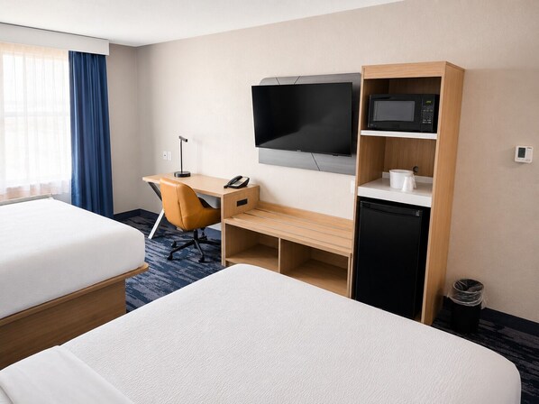 A hotel room with two beds, a desk with a chair, a TV, a microwave, and a coffee maker.