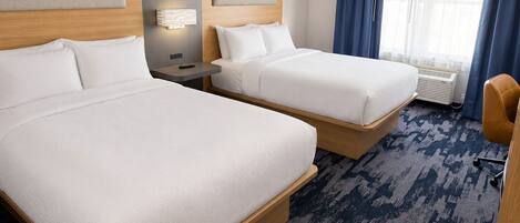 A hotel room with two beds, a nightstand, a lamp, an air conditioning unit, and a view of the outdoors through a window with blue curtains.