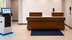Una reception con una postazione digitale self-service, un telefono e un tappetino blu in un'accogliente hall moderna.