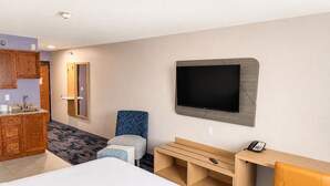 Una camera d'albergo con un letto, una televisione, una scrivania, una sedia, un telefono e un bagno.