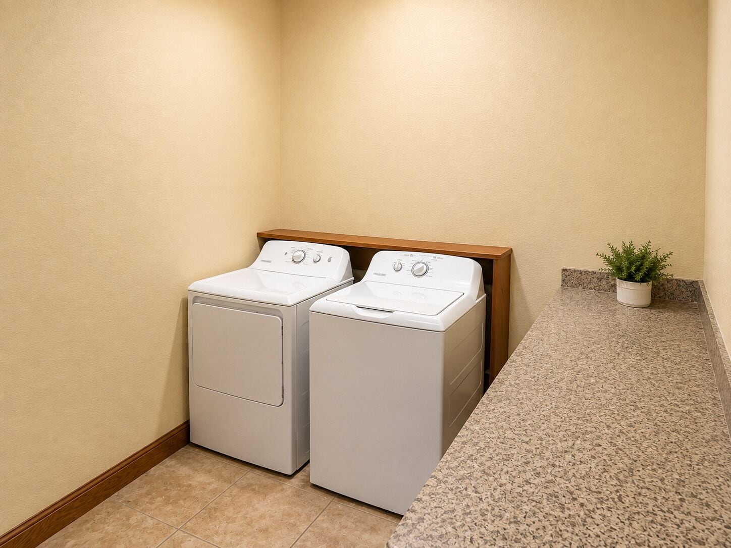 A laundry area with two front-loading washing machines and a wooden shelf above them.