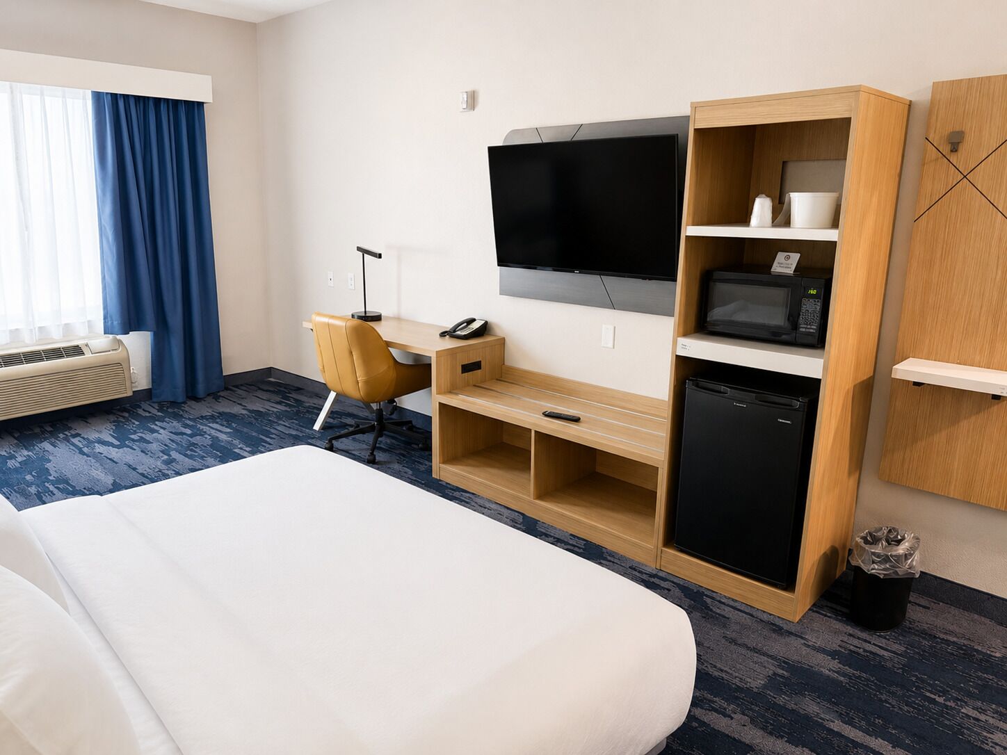 A hotel room with a bed, a desk with a chair, a television, a microwave, and a refrigerator.