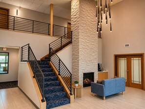 A spacious interior with a staircase, a fireplace, a blue sofa, and a stone accent wall.