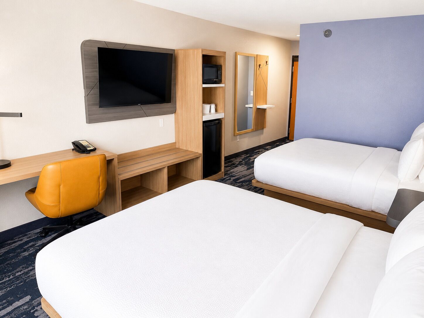 A hotel room with two beds, a desk, a chair, a TV, and a wardrobe.