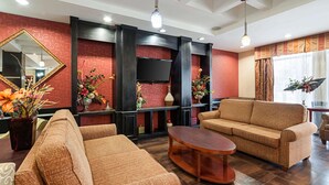 A modern living room with a sofa, armchairs, and a coffee table. There is a flat-screen TV mounted on the wall, a large mirror, and decorative plants. - Comfort Suites Sulphur - Lake Charles (Sulphur)