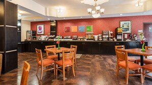 A modern hotel lobby with a central counter, wooden tables and chairs, and a red patterned wall. - Comfort Suites Sulphur - Lake Charles (Sulphur)