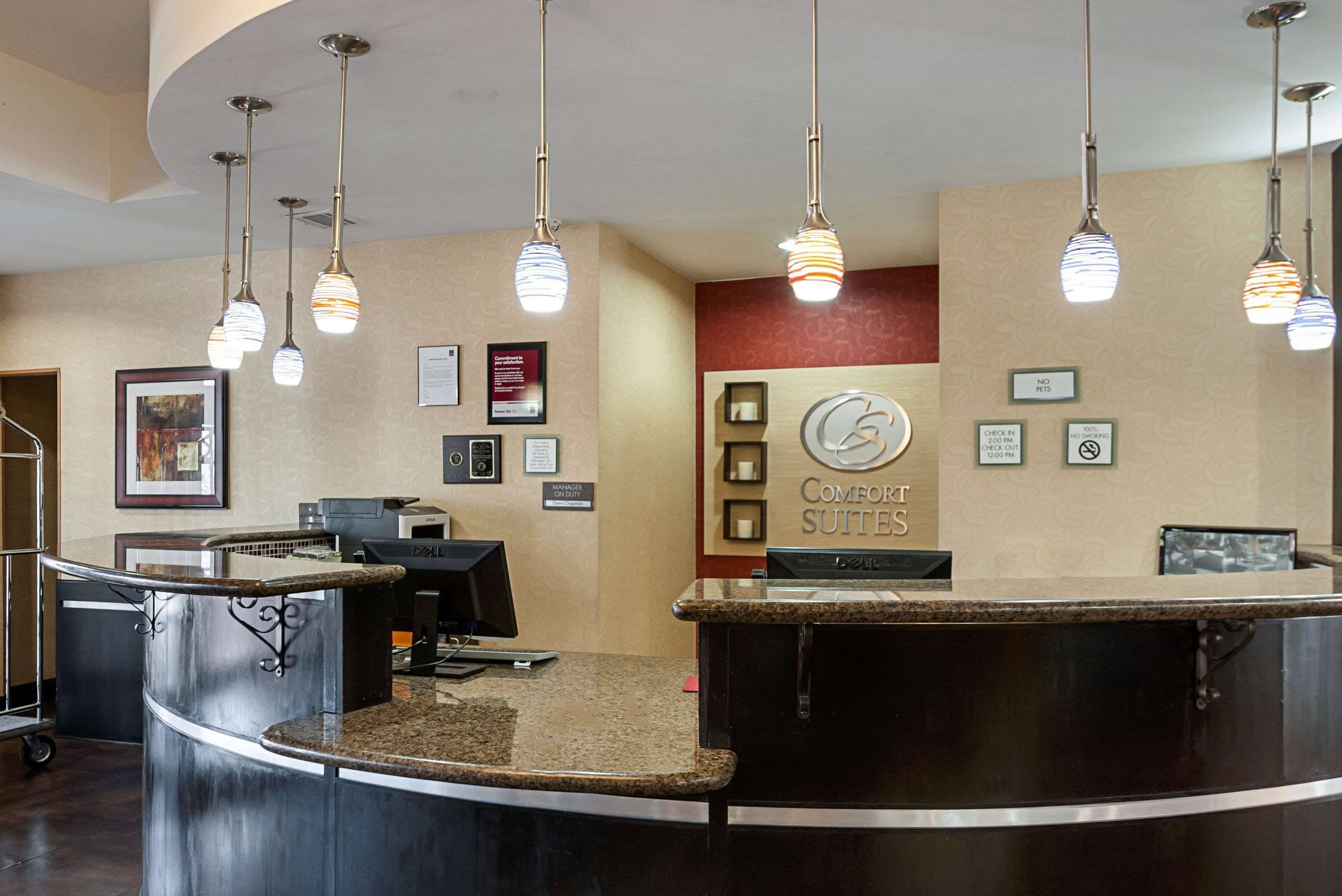 A hotel reception area with a curved counter, multiple framed pictures on the wall, and a sign for Comfort Suites.