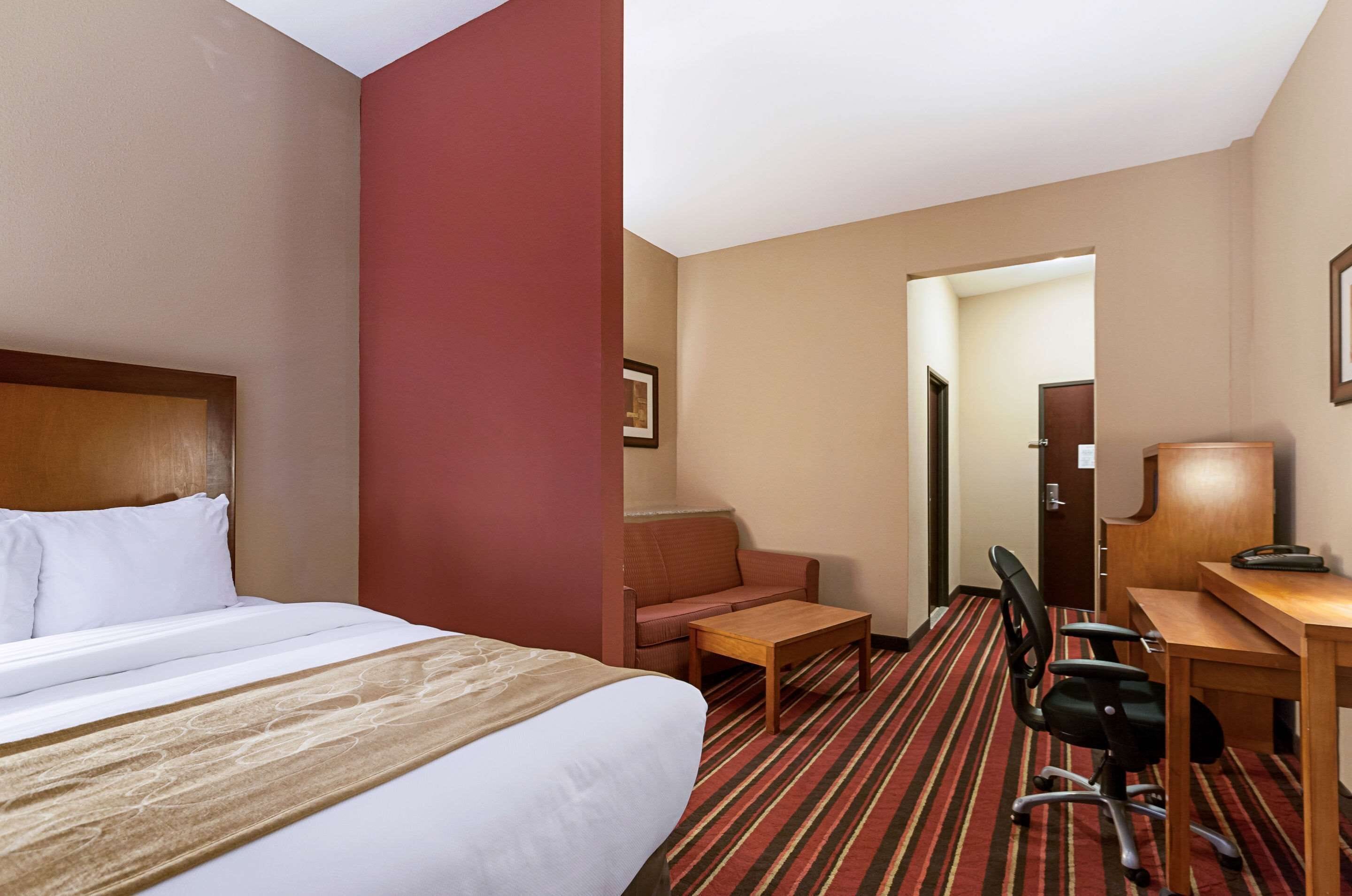 A hotel room with a bed, a desk, a chair, and a small table.