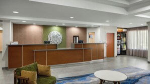 A hotel reception area with a reception desk, a green sofa, a round table, and a large window with curtains. - Fairfield Inn & Suites South Boston (South Boston)