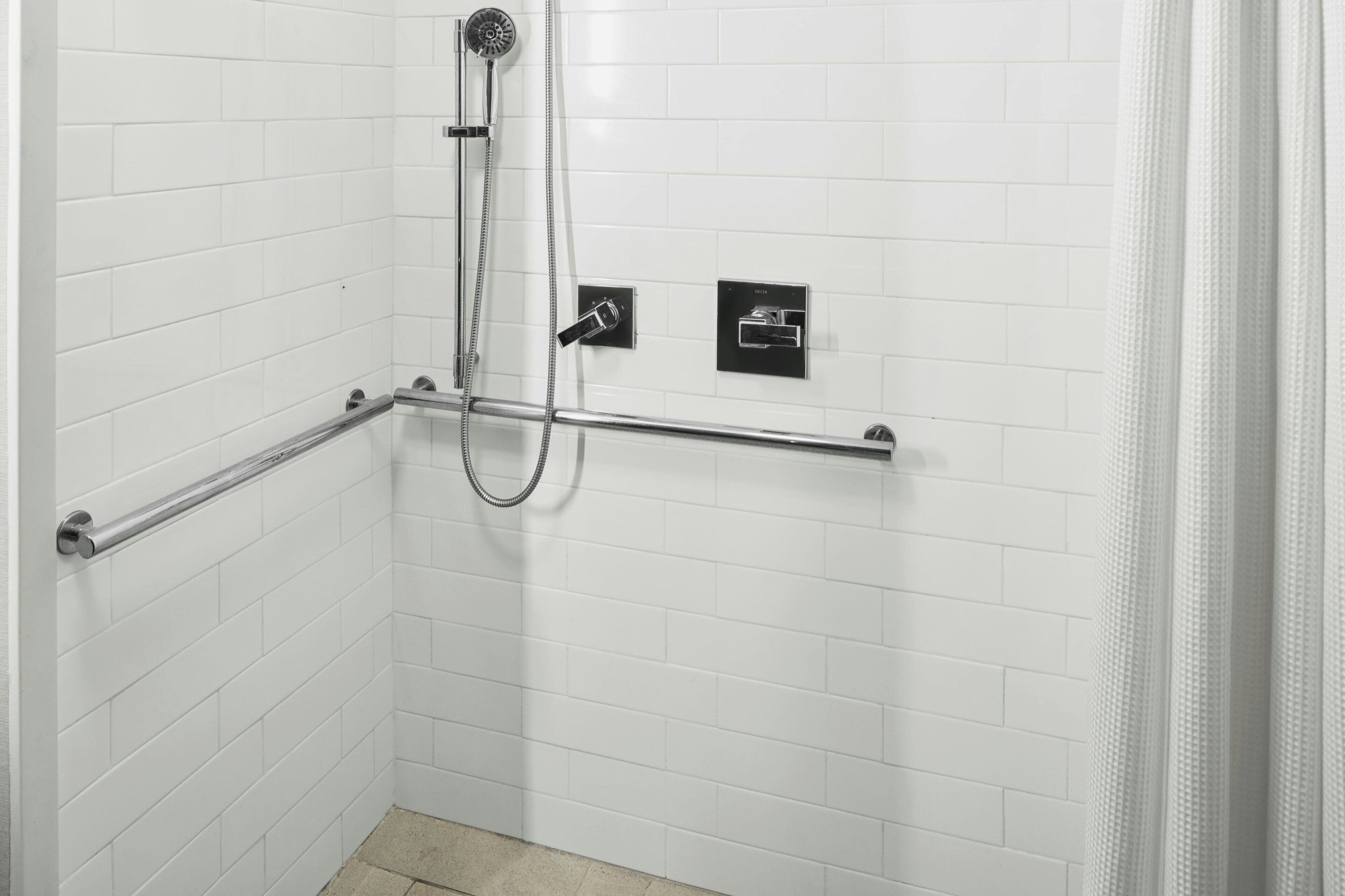 A white tiled shower area with a handheld showerhead, a handheld shower attachment, and a control panel.