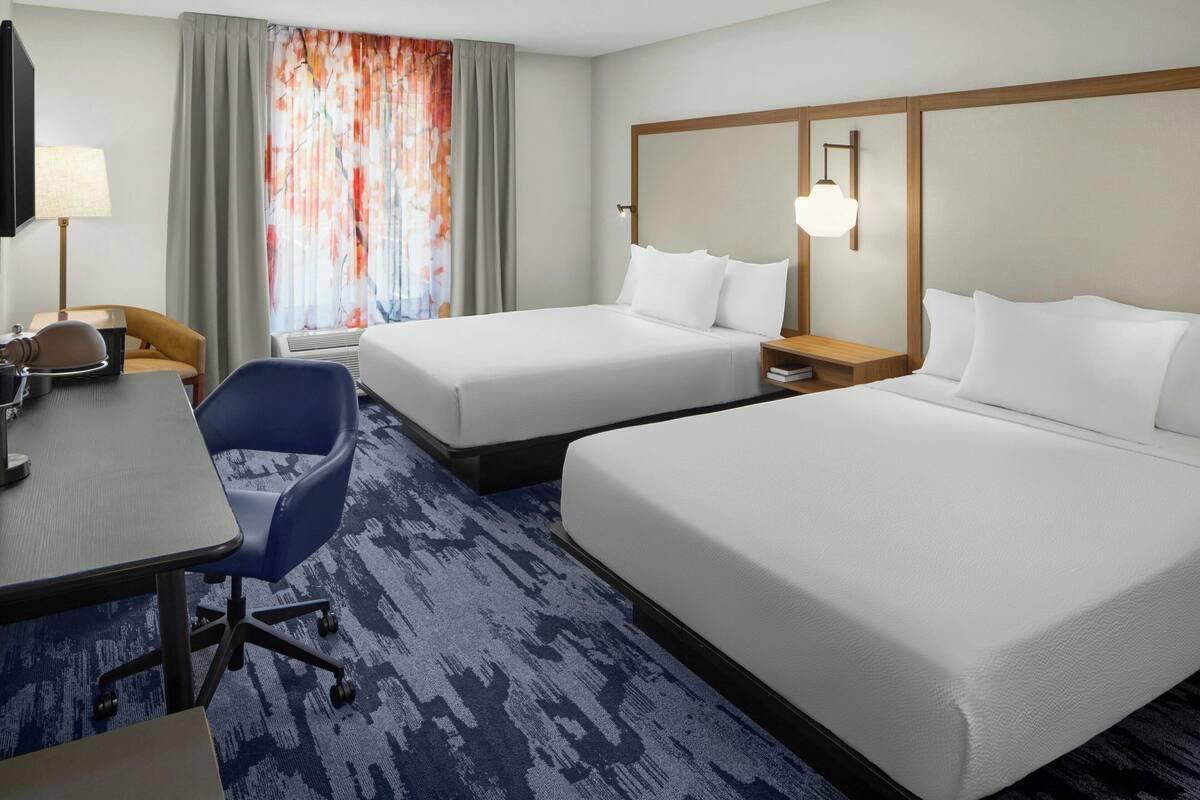 A hotel room with two beds, a desk, a chair, a TV, and a window with curtains.