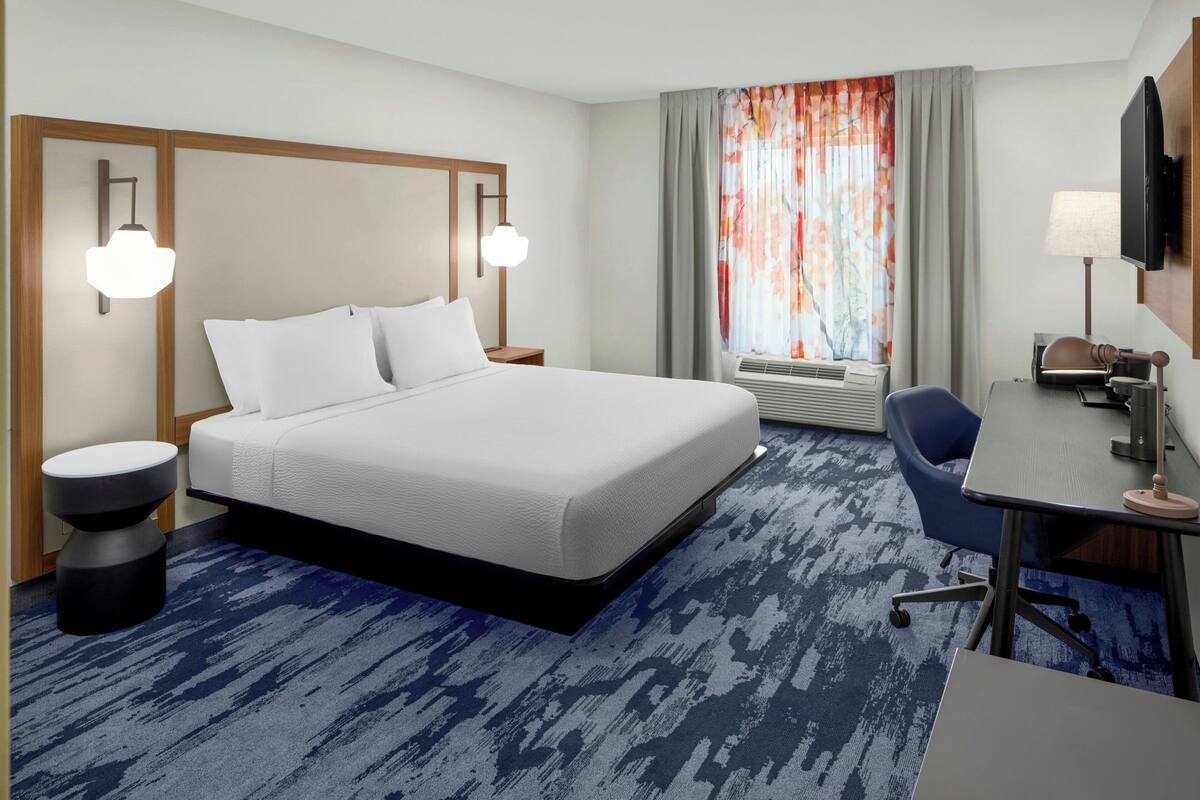 A hotel room with a large bed, a desk with a chair, a TV, and a window with curtains.
