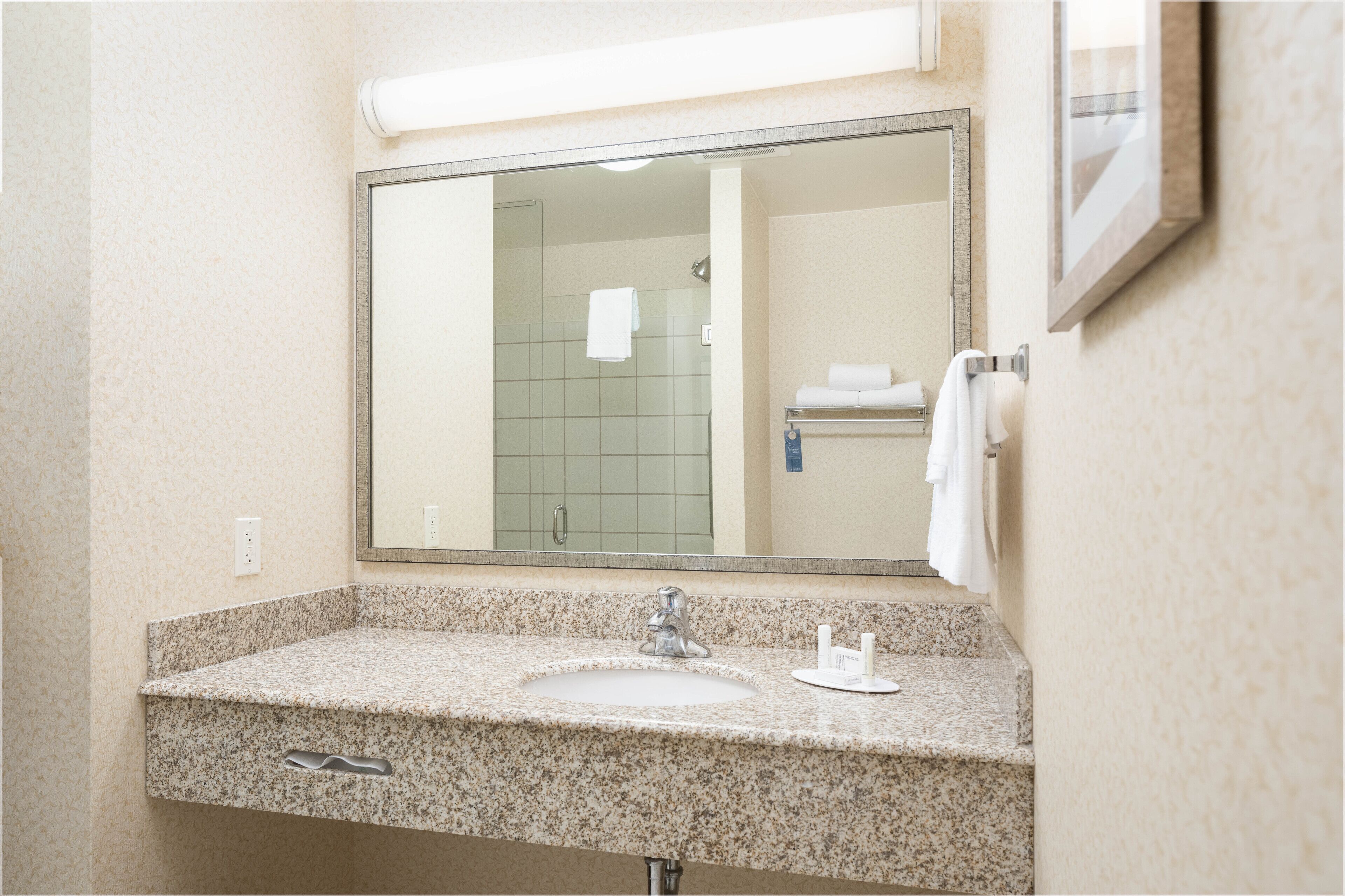 A bathroom with a granite countertop, a sink, a mirror, and a towel rack.