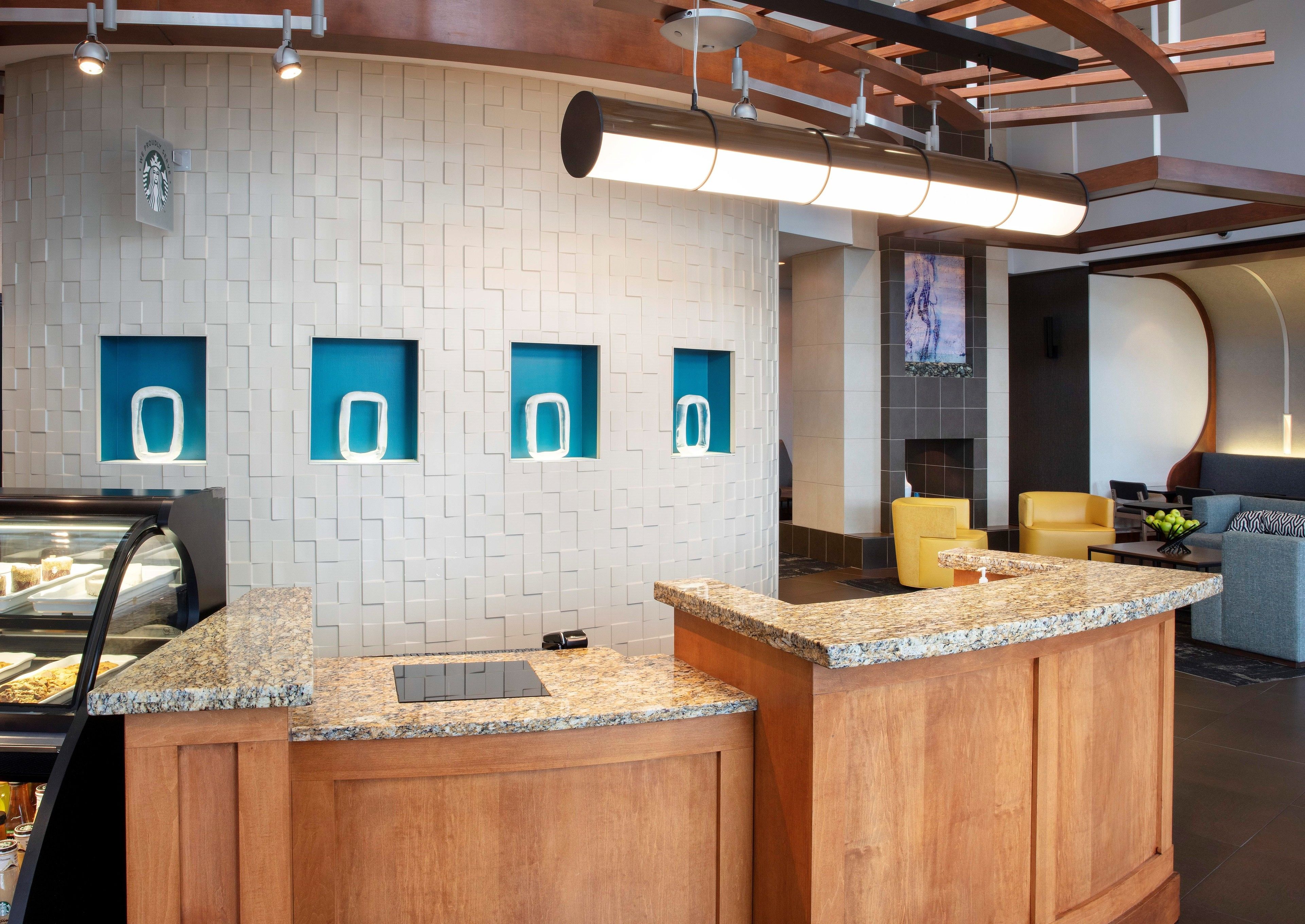 A modern reception area with a wooden counter, a coffee machine, and a display case with pastries.